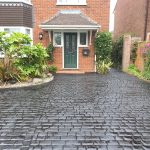 Image showing a pattern imprinted concrete driveway with a dark grey finish and cobblestone effect pattern with a house and garden plants adorning the front