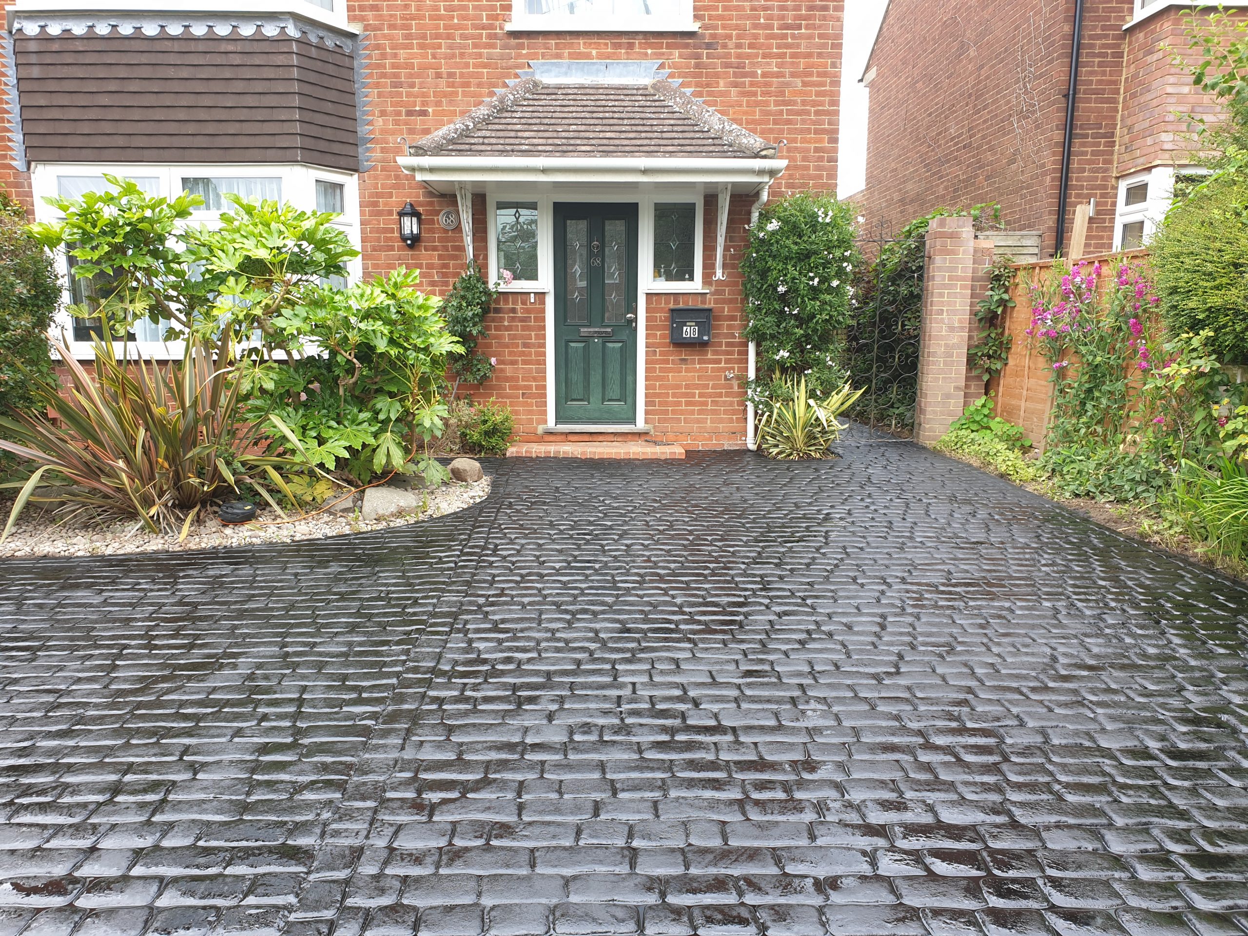 Image showing a pattern imprinted concrete driveway with a dark grey finish and cobblestone effect pattern with a house and garden plants adorning the front