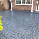 Image showing a pattern imprinted concrete driveway with a grey finish and cobblestone effect pattern with the front of the house in view partially